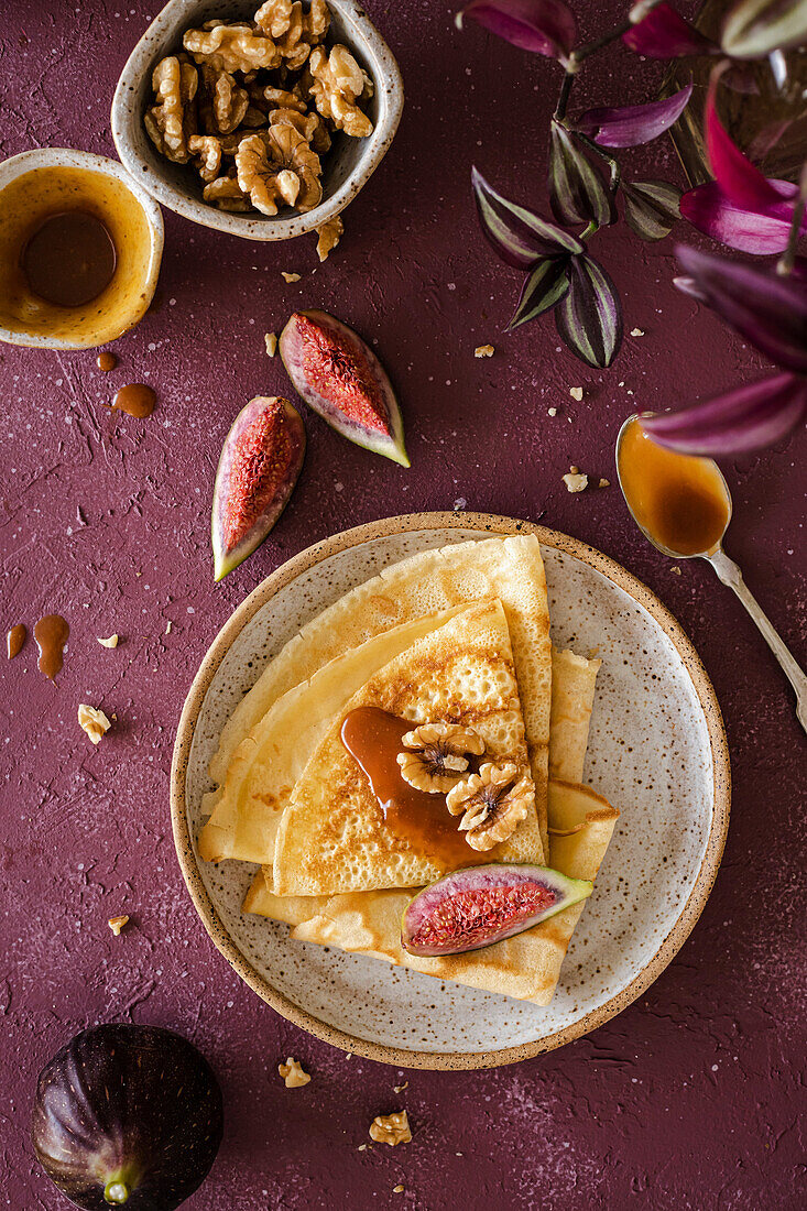 Crepes, folded on a handmade ceramic plate, decorated with figs, caramel and walnuts on a purple background