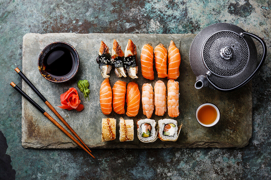 Sushi-Set mit Tee, serviert auf grauer Steinplatte auf Metallhintergrund