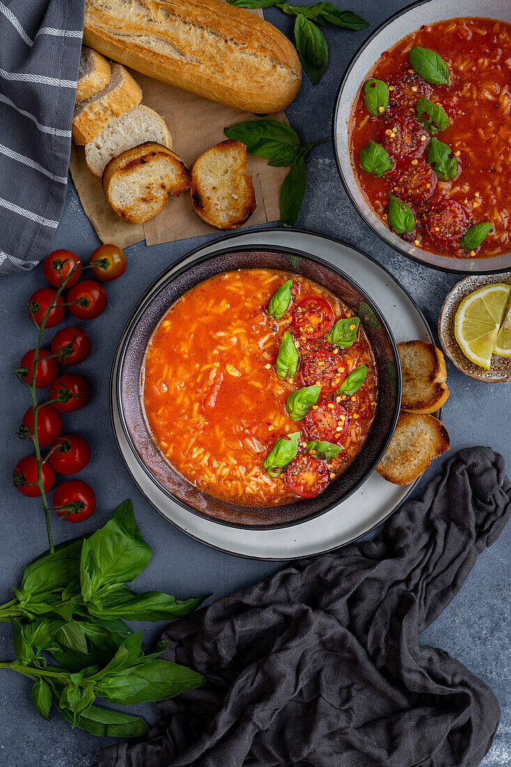 Tomaten-Reis-Suppe garniert mit Kirschtomaten und Basilikumblättern in zwei Schüsseln vor einem dunklen Hintergrund