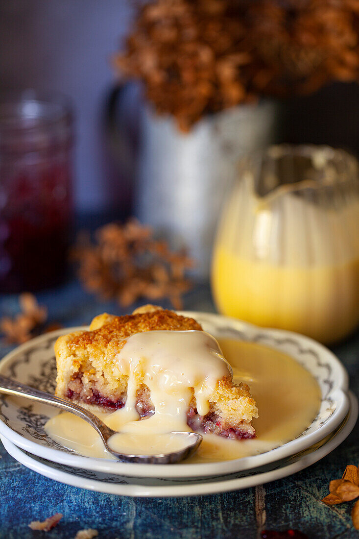 A slice of British custard tart with breadcrumbs and jam, served with custard on top