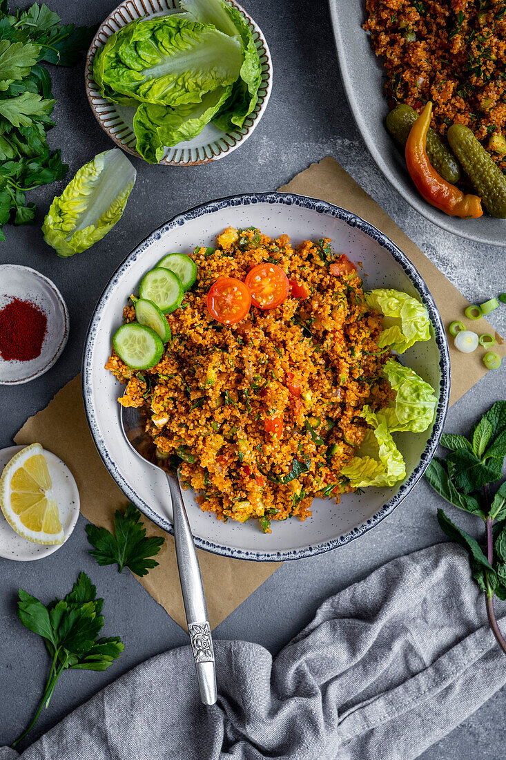 Turkish bulgur salad in a white bowl with lettuce leaves, tomato slices and cucumber on top