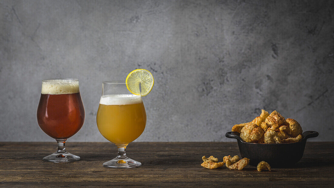 Ein Weizen- und ein Braunbier, in Tulpengläsern auf Holztisch mit Schale mit Schweineschwarten