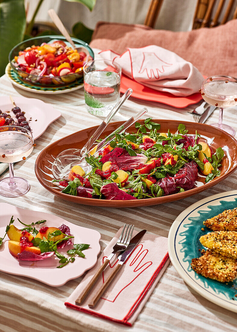 Ein Picknick mit Salat an einem Tisch im Freien, mit frischem Obst und Gebratenem, auf einem gestreiften Tischtuch