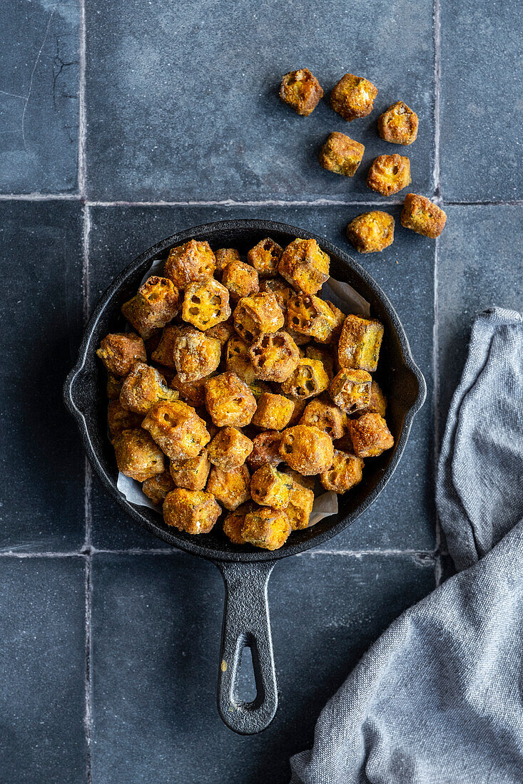 Breaded fried okra in a small cast-iron pan, photographed against a grey background