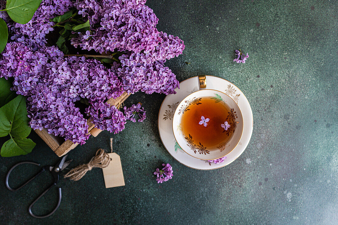 Delicious black tea in white vintage cup on mint green concrete table with aromatic lilac flowers