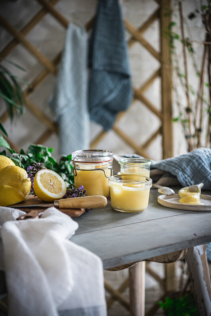 Hausgemachter Lemon Curd in Gläsern, umgeben von Zitronen in einer rustikalen Küche