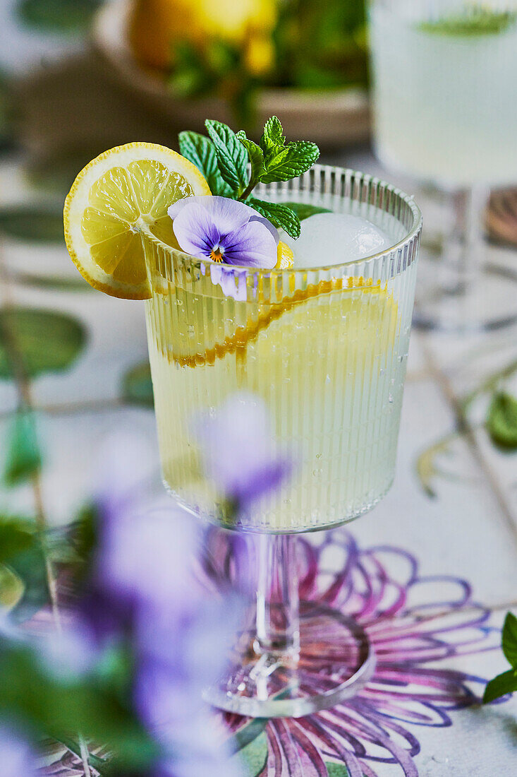 Lemon-mint lemonade mocktail on a floral background with lemon, mint and purple flower decoration