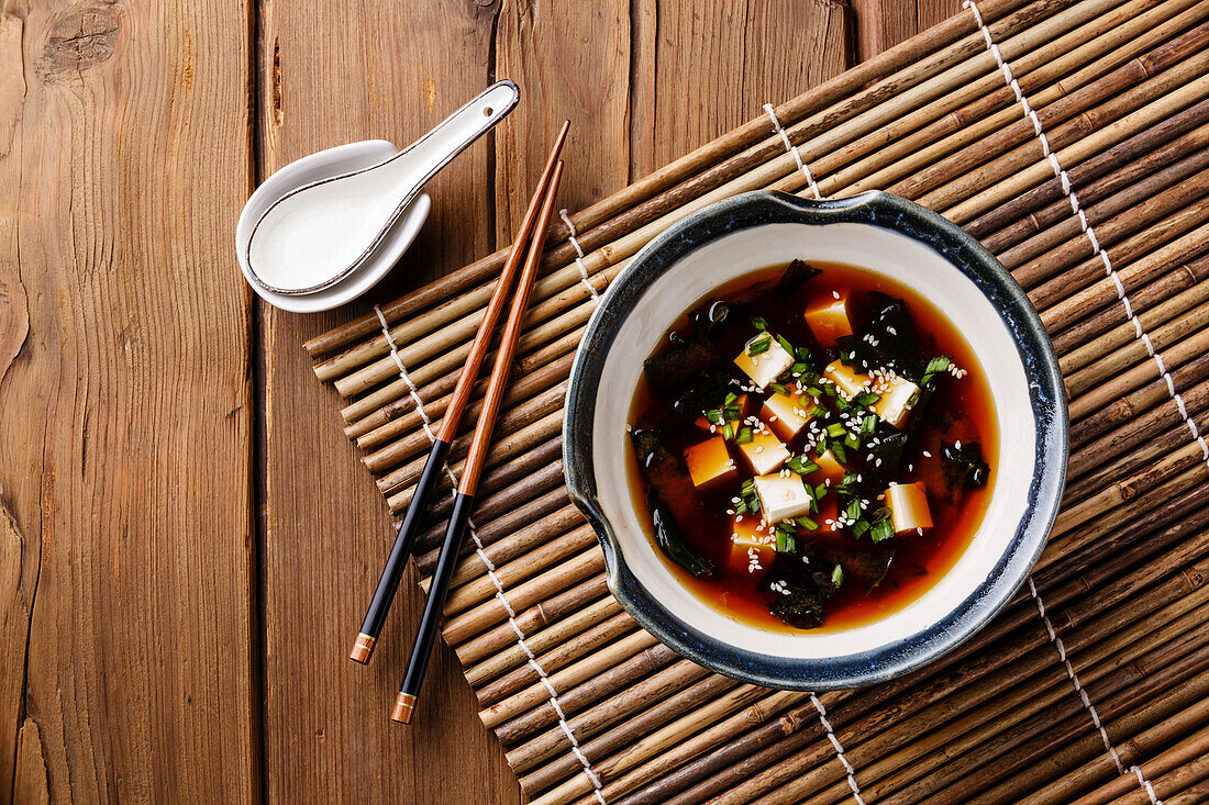 Miso-Suppe mit Tofu, Seetang und Sesam in Schale auf Holzuntergrund