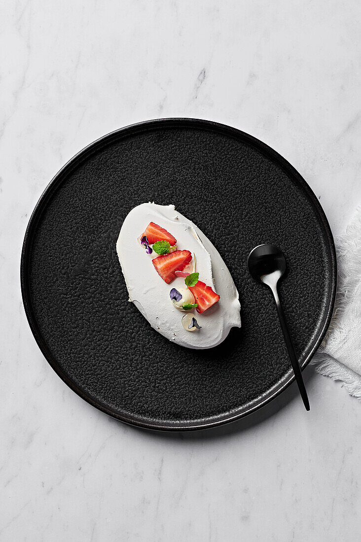 Meringue with yoghurt mousse, macerated strawberries and bergamot gel from above on a black plate