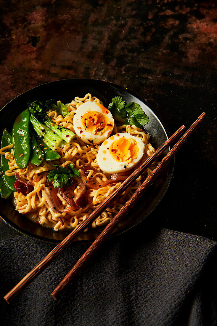 Egg and vegetable noodles in bowl with chopsticks and black napkin