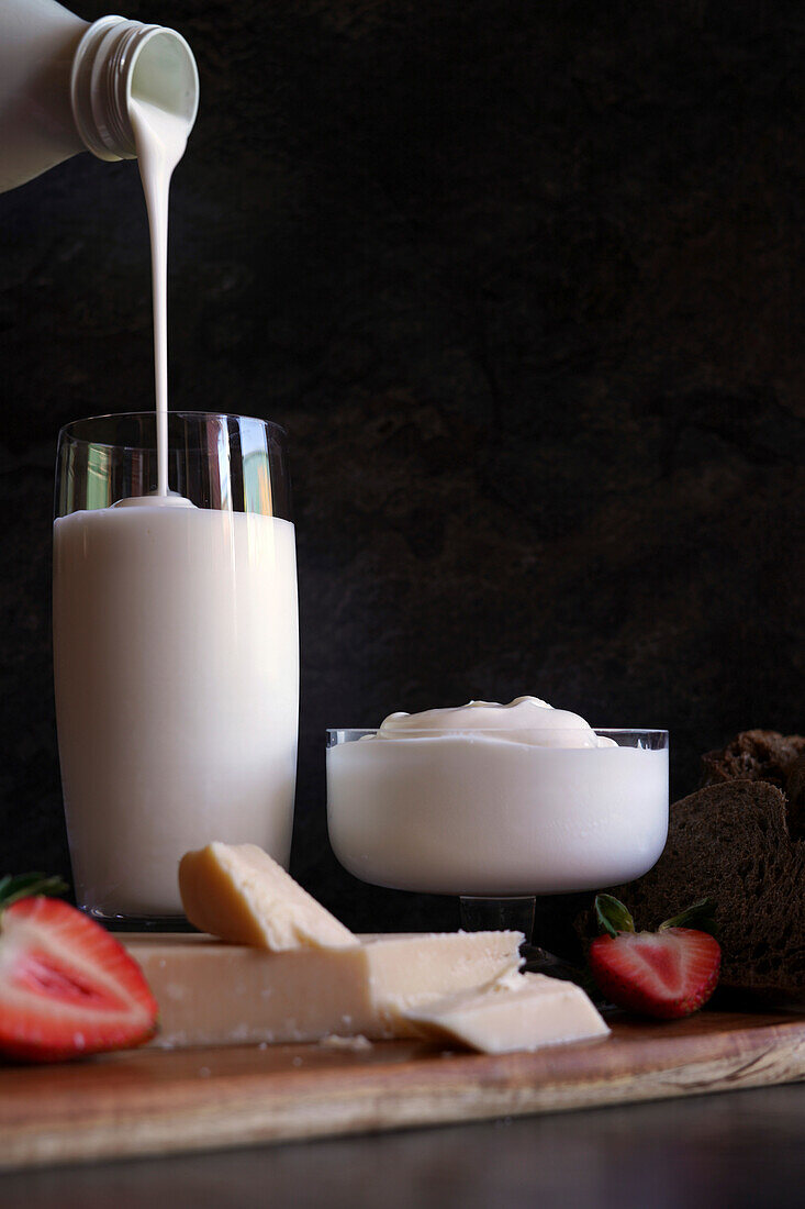 Healthy probiotic dairy, including kefir, Greek style yoghurt, and parmgiano reggiano. Pouring kefir from bottle.