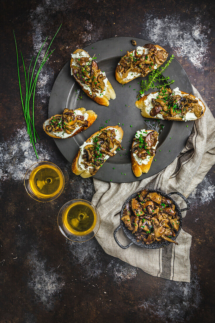 Mushroom and goat cheese crostini arranged on a pewter plate, with sherry in glasses, mushrooms in small dish