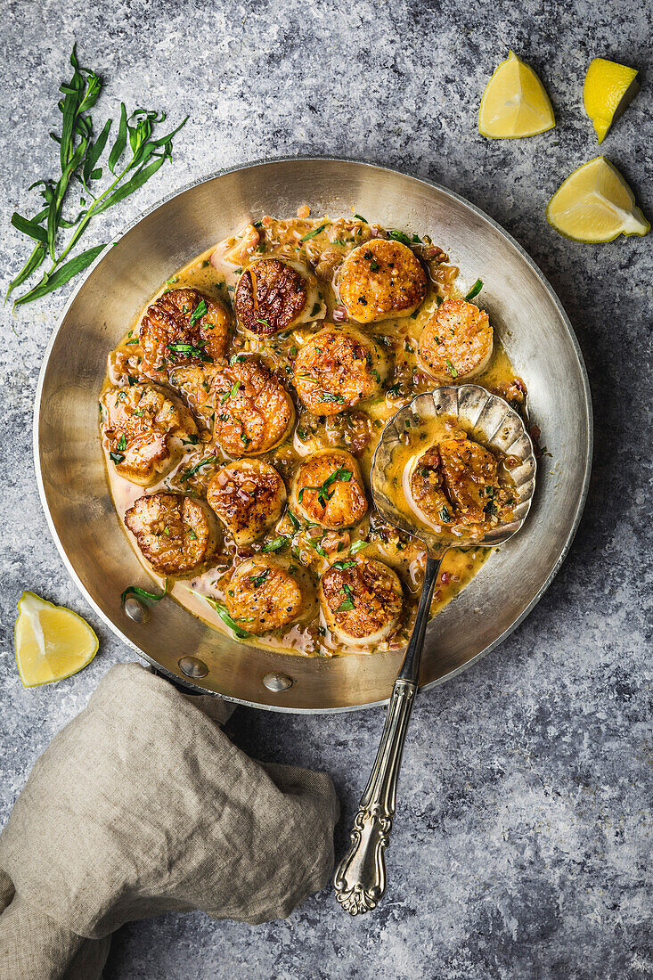 Gebratene Jakobsmuscheln mit brauner Buttersauce in der Pfanne mit Estragon und Zitrone, mit Leinenserviette