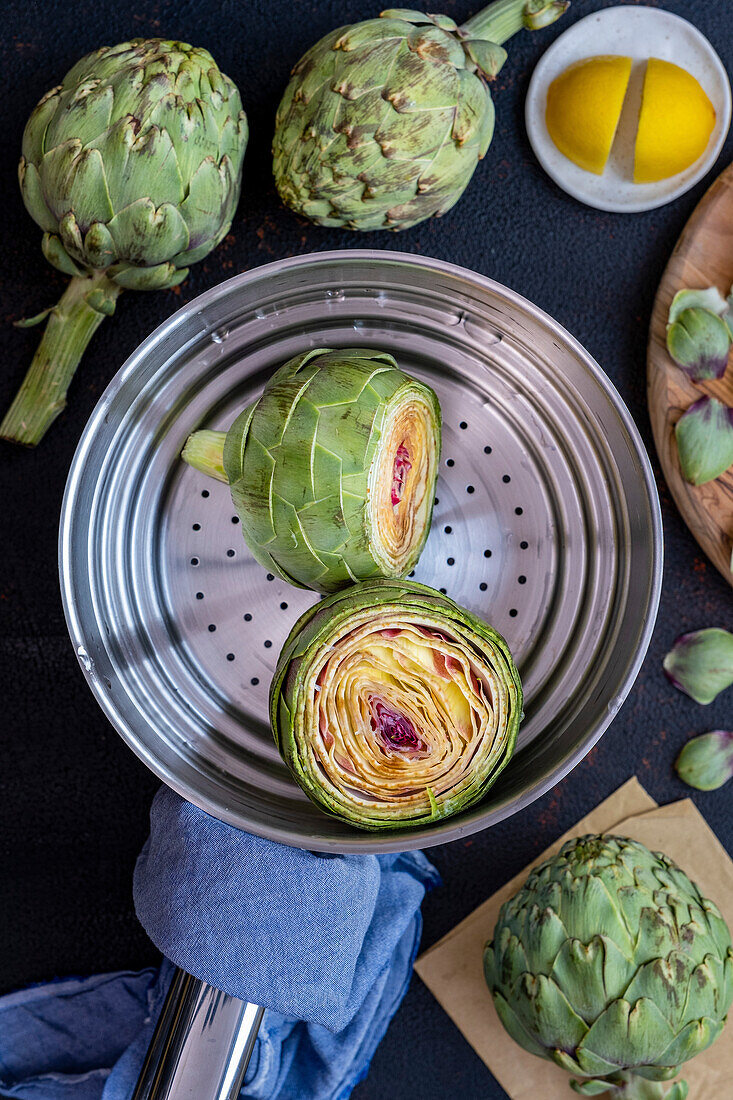 Artichokes in a steaming basket, with more artichokes and lemon halves