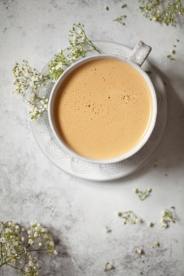 A latte in a mug with a frothy top. The mug is surrounded by white flowers