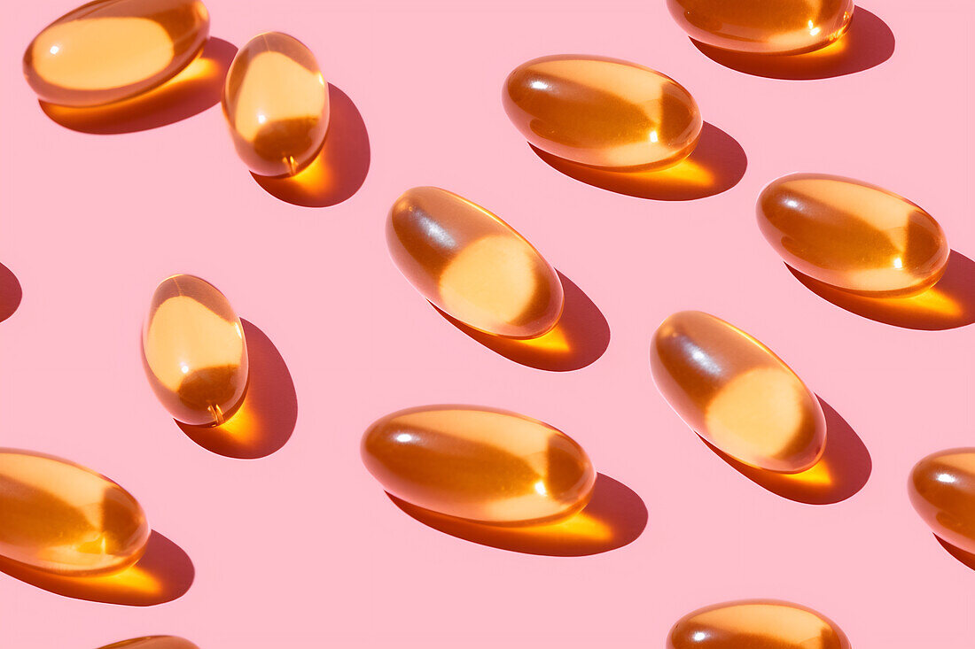 Composition of orange vitamin pills scattered on a pink background in a bright studio