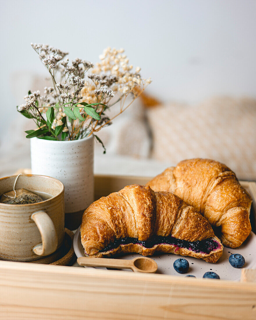 Breakfast in bed with freshly baked croissants with blueberry jam and tea in a mug