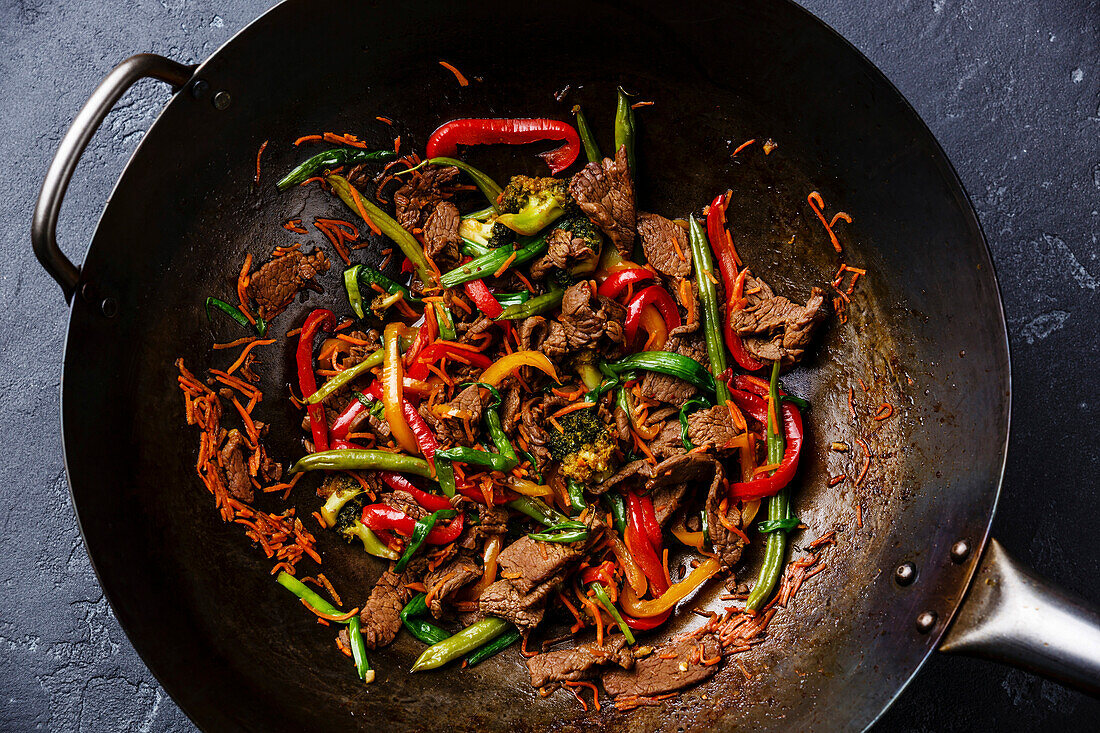 Gebratenes Rindfleisch mit Gemüse in Wok-Pfanne auf dunklem Hintergrund Nahaufnahme
