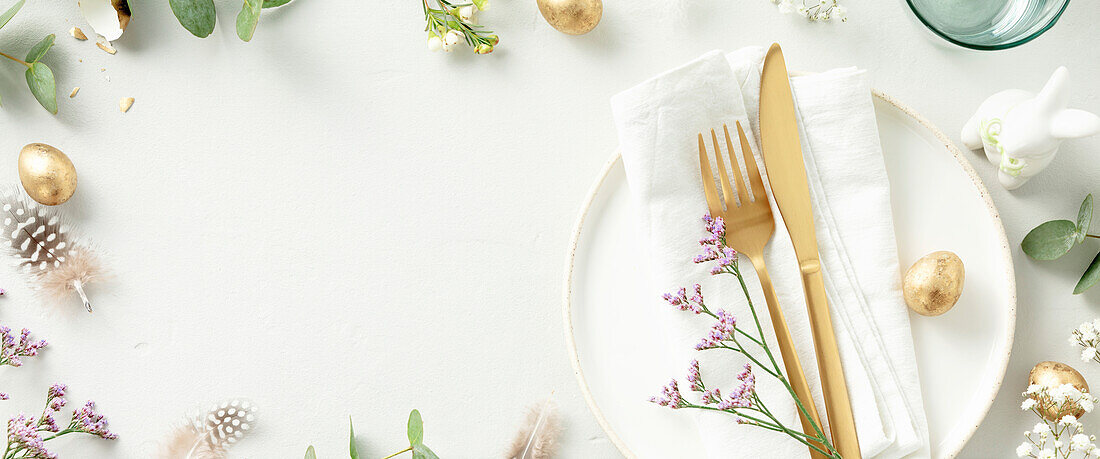 Ostern Tischdekoration. Stilvolle Osterbrunch-Tischdekoration mit weißem Teller, Serviette, goldenem Besteck, Ostereiern und Frühlingszweigen auf hellgrauem Hintergrund in der Draufsicht copy space