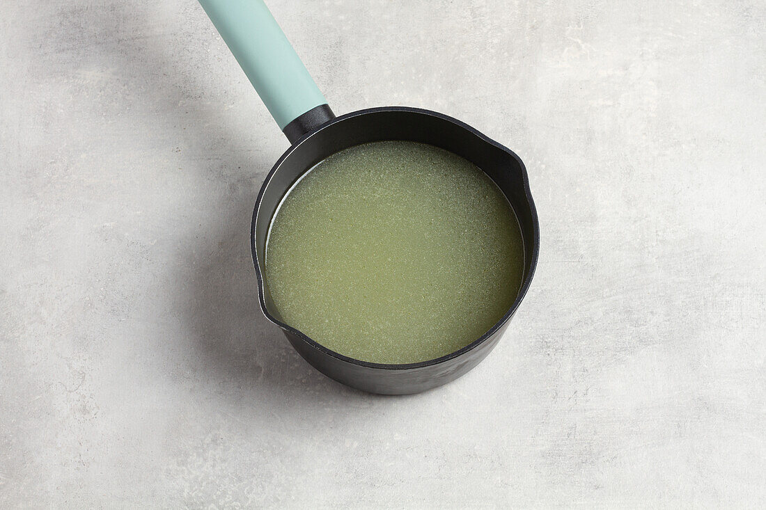 Black pan with blue handle in round shape with green watery broth on grey table seen from above