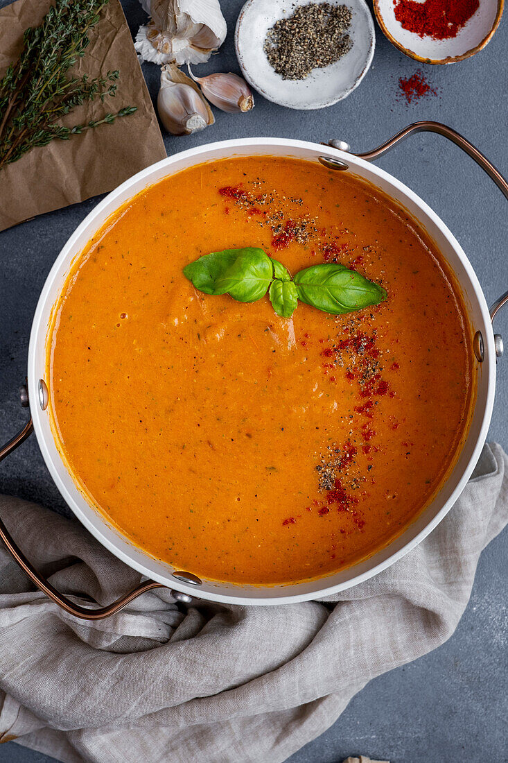 Roasted tomato soup in a pot, garnished with spices and fresh basil leaves, with black pepper, paprika, garlic and thyme