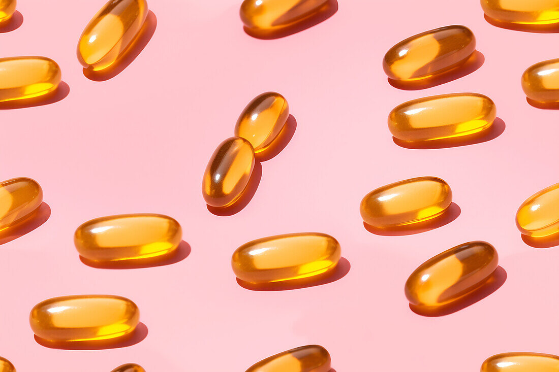 Composition of orange vitamin pills scattered on a pink background in a bright studio