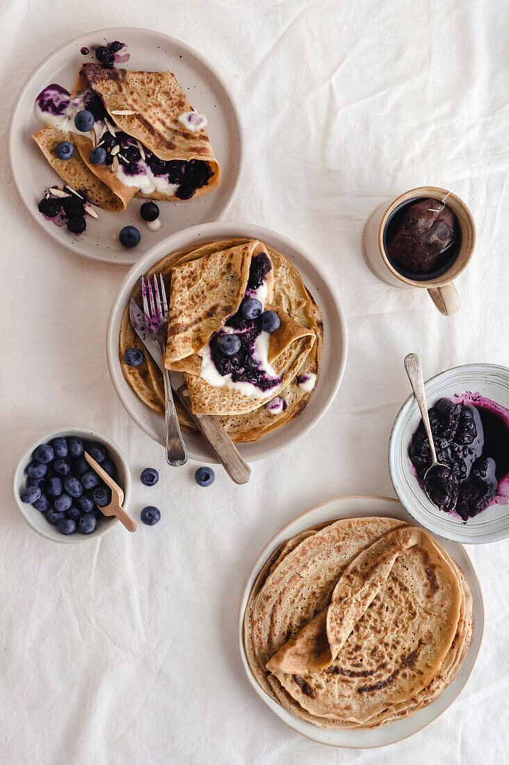 Crepes mit Blaubeermarmelade und Joghurt an einem Tisch mit leichter Atmosphäre, Frühstück