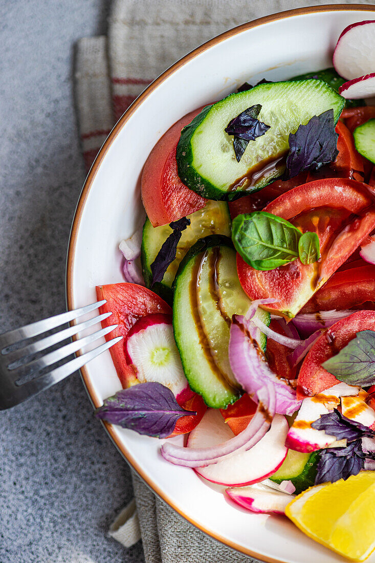 Tall, flavoursome vegetarian salad with cucumber, lemon, onion and tomato with green leaves and dressing in a bowl on the table