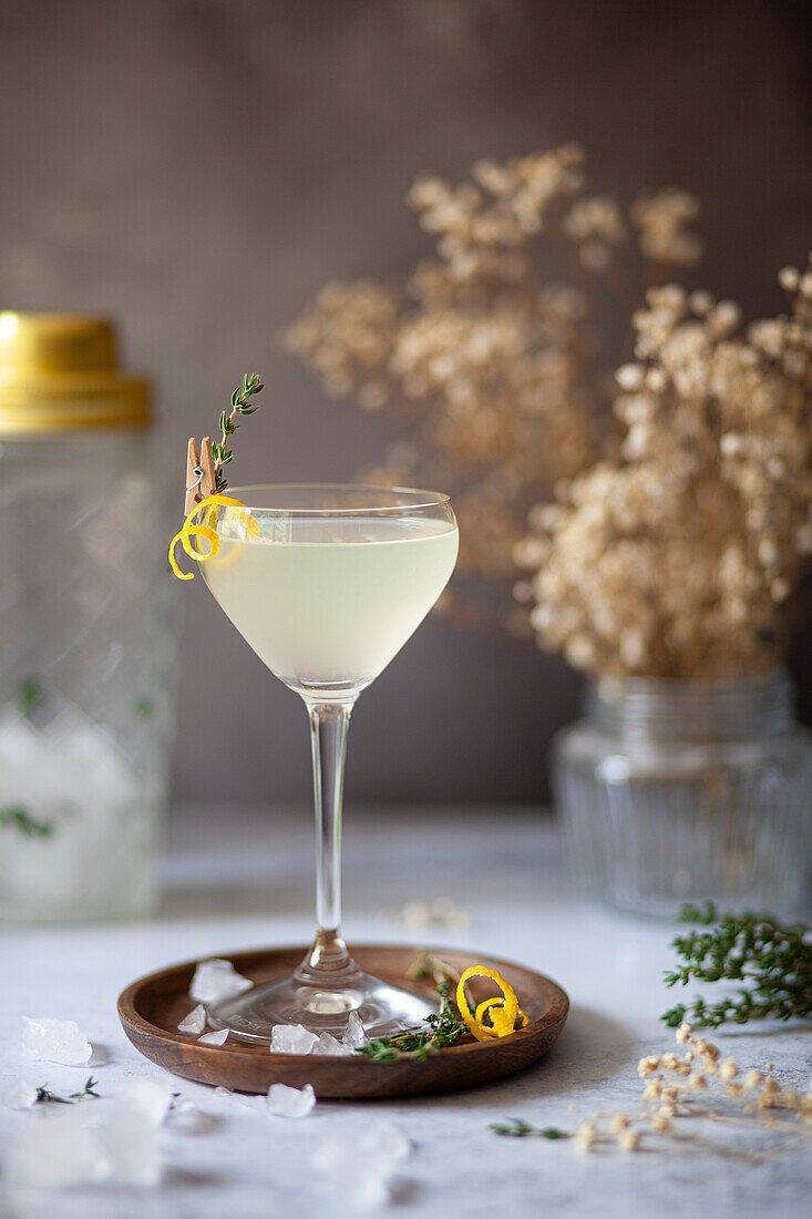 A vodka amd lemon cocktail served in a Nick and Nora glass and garnished with a lemon zest spiral and fresh thyme.