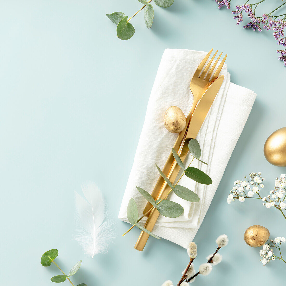 Easter table decoration. Stylish Easter brunch table with eggs, golden cutlery and spring branches on blue background top view flat lay