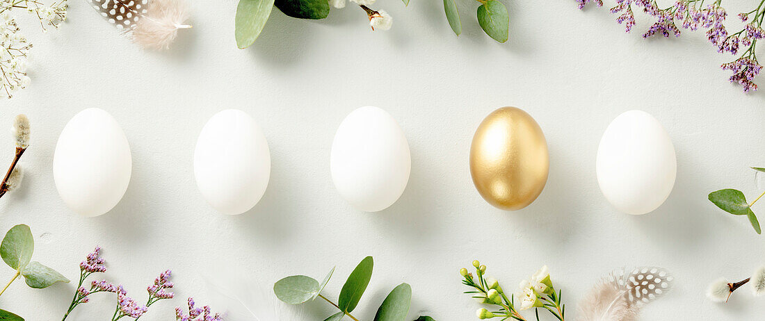 Easter decoration. Happy Easter concept with golden Easter eggs, feathers and spring flowers on blue background. Flat lay banner