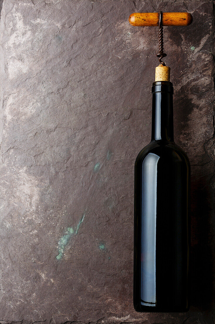 Wine bottle and corkscrew on stone slate background