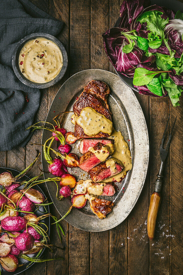 Sliced steak au poivre with cream sauce and roasted radishes on a metal plate