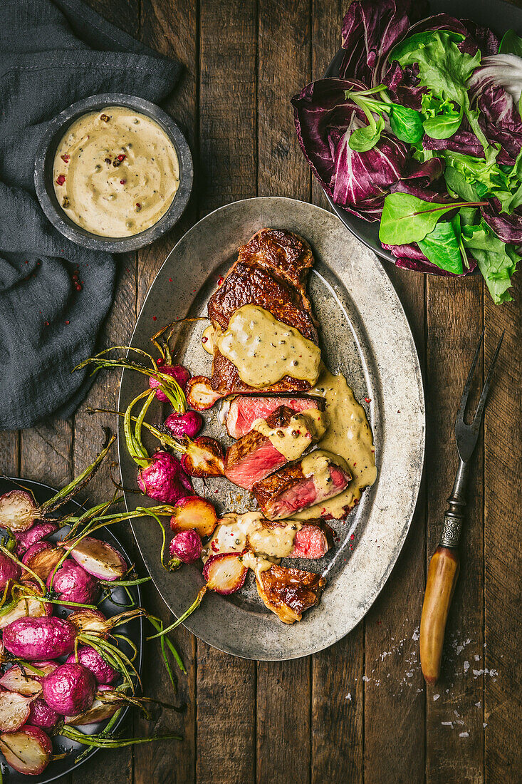 Steak au poivre in Scheiben geschnitten mit Sahnesauce und gerösteten Radieschen auf Metallteller