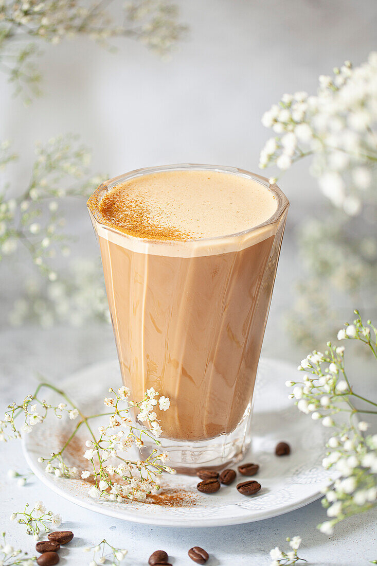 A modern heatproof glass filled with vegan latte coffee drink and topped with a dusting of ground cinnamon spice.