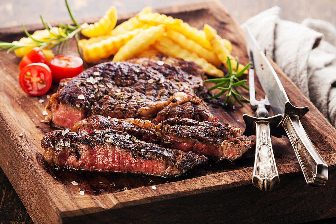 Sliced, medium rare grilled Black Angus ribeye steak with chips on a serving board block