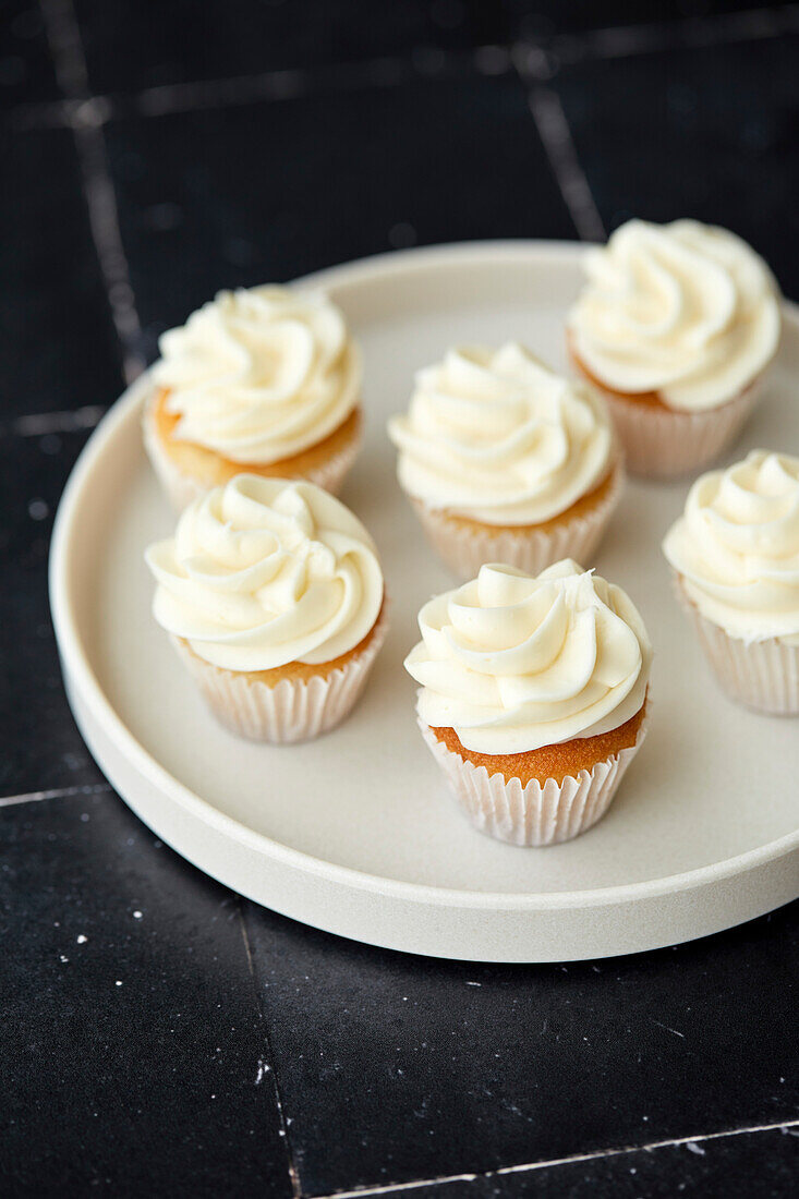 Mini-Vanille-Cupcakes auf einem weißen Teller und schwarzem Kachel-Hintergrund
