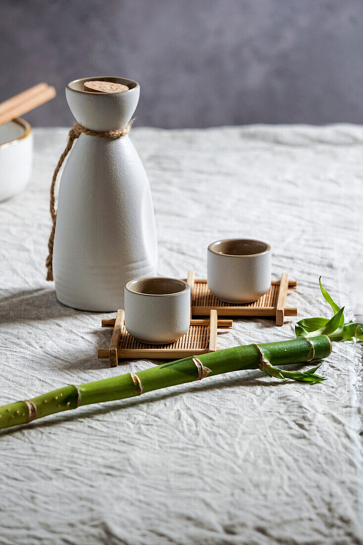Japanisches Sake-Stillleben mit einem Bambuszweig, heller Leinenhintergrund, asiatische Zeremonie