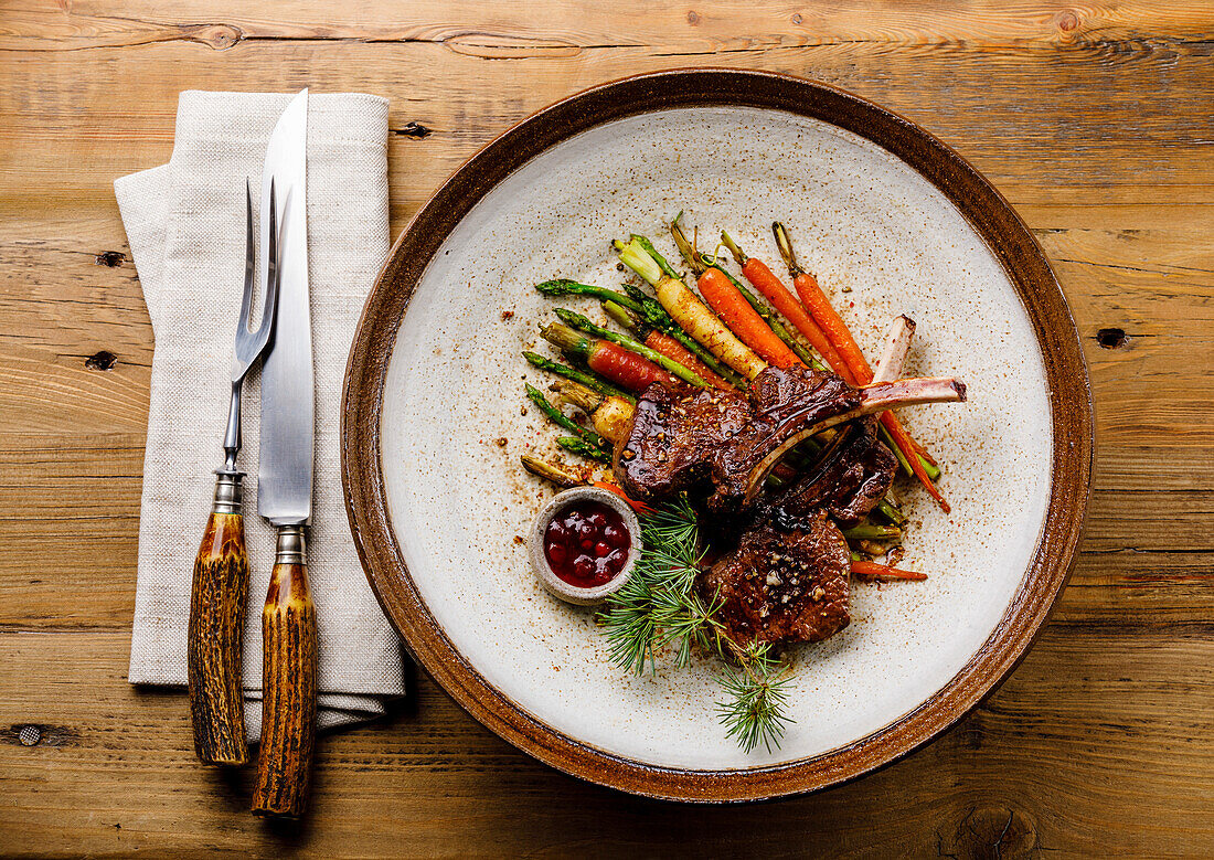 Grilled venison ribs with baked vegetables and berry sauce on a wooden background