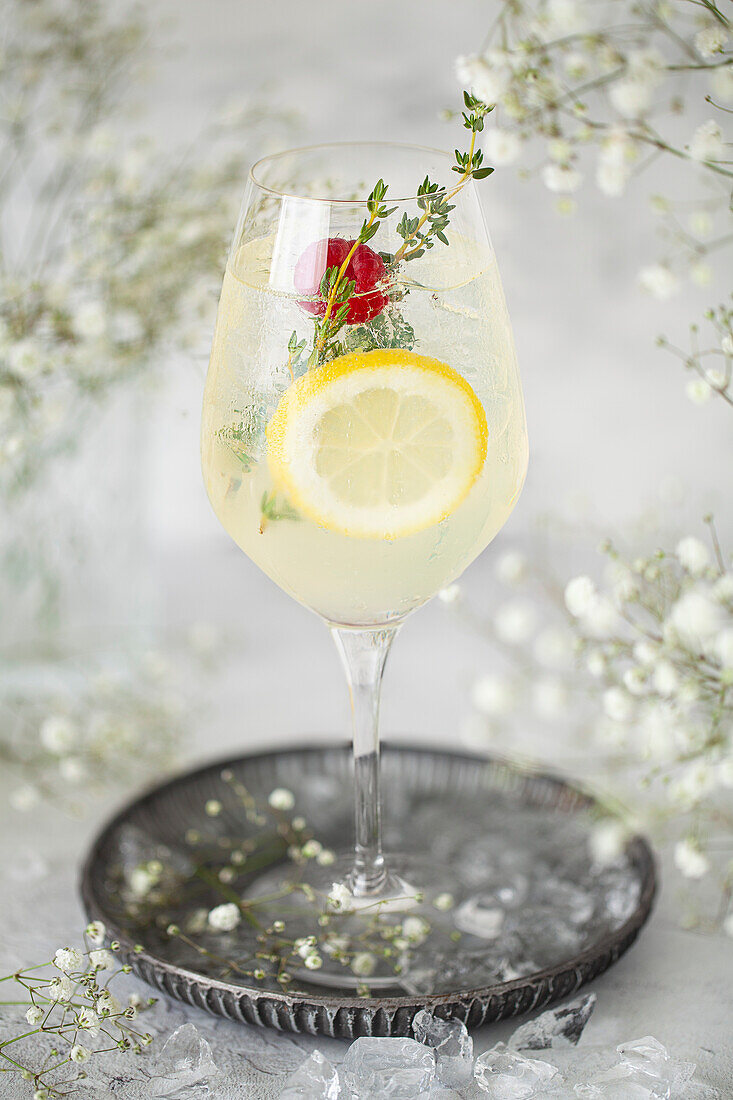 A sparkling lemon cocktail with fresh lemon slices, raspberries and thyme on a tray with ice