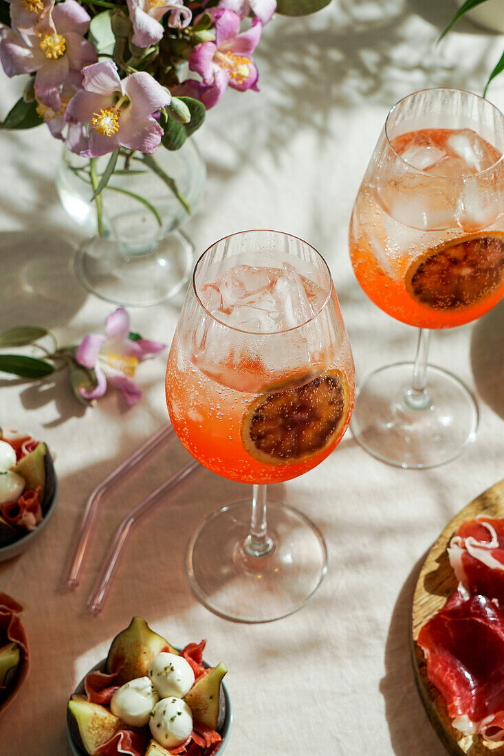 Aperol Spritz-Cocktail, auf zartrosa Leinentischdecke, Schatten, Sonnenlicht, Sommerdrink im Glas