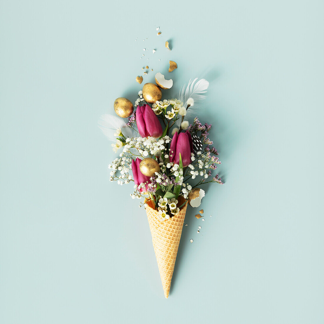 Easter composition. Ice cream cone with beautiful flowers and golden Easter eggs laid flat on blue background