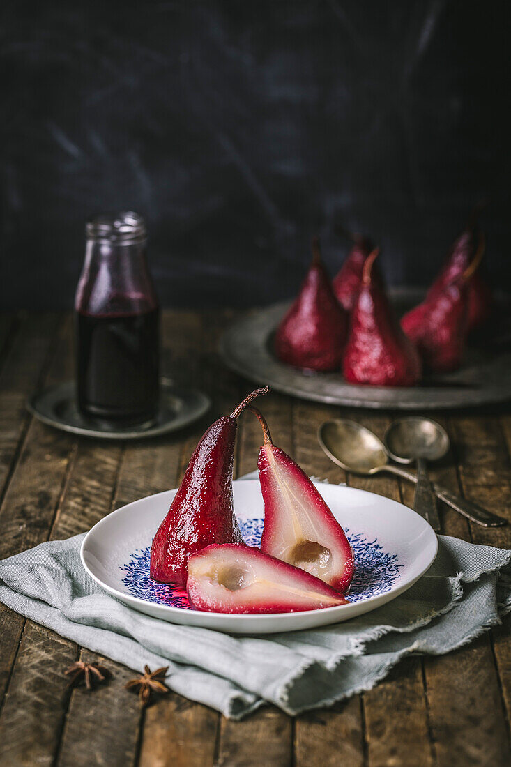 Pears poached with red wine, sliced on a white and blue plate with pears in the background