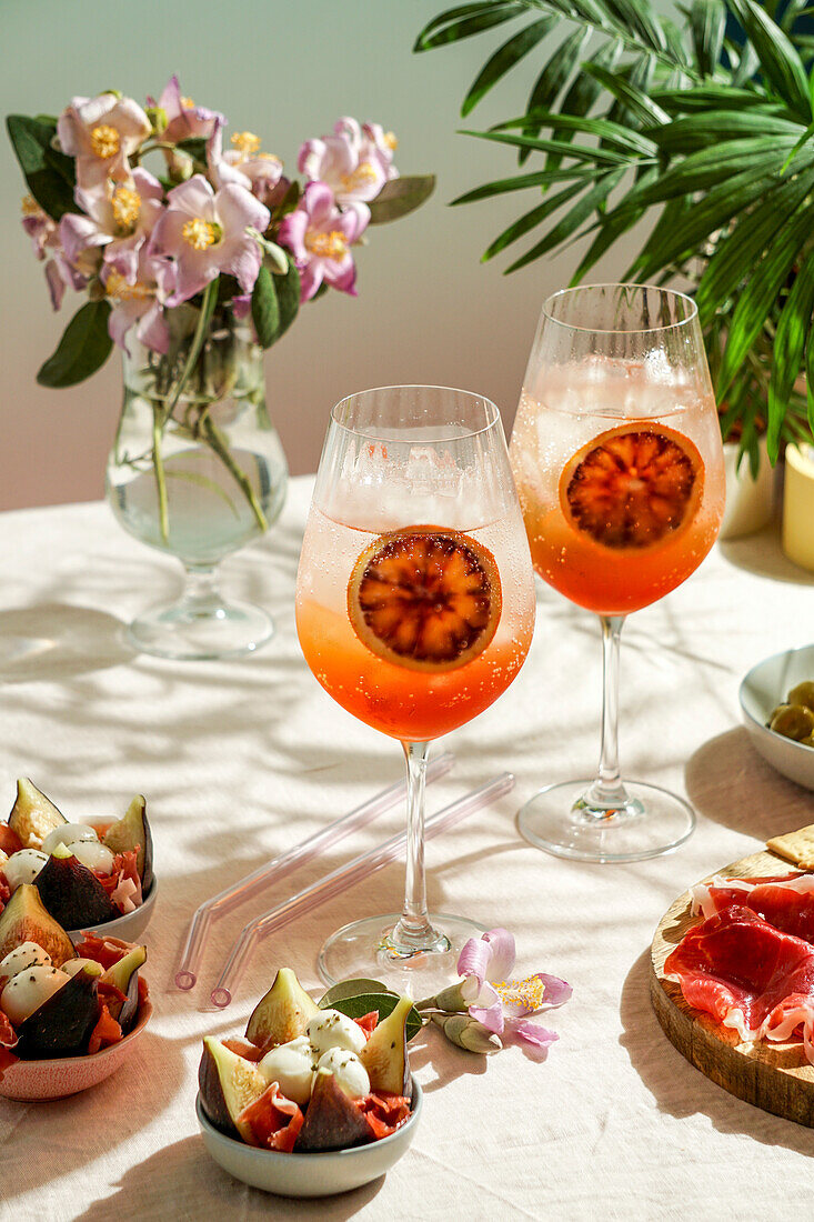 Aperol Spritz-Cocktail, auf zartrosa Leinentischdecke, Schatten, Sonnenlicht, Sommerdrink im Glas