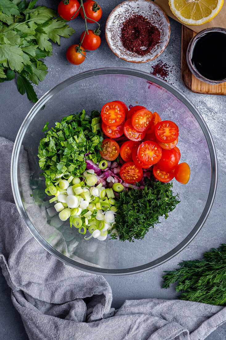 Chopped onions, green onions, parsley, dill and halved cherry tomatoes in a glass bowl