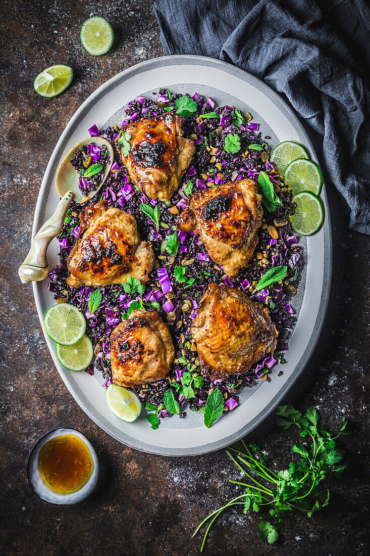 Glazed, fried chicken pieces on black rice and red cabbage salad on an oval platter with lime wedges