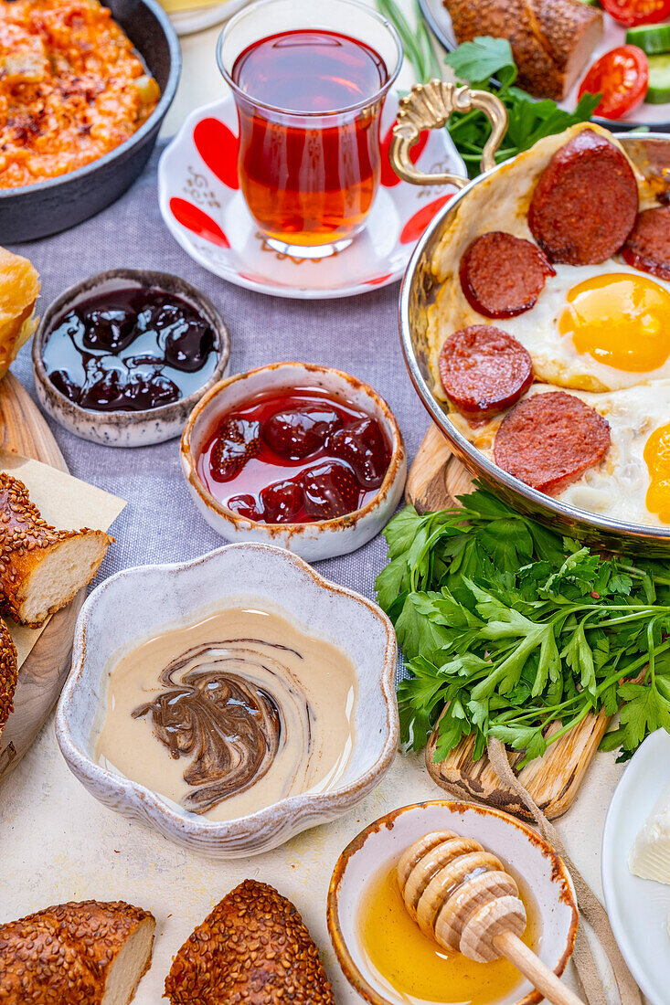 Tahini pekmez in a bowl and other Turkish breakfast dishes such as jams, eggs and sujuk, menemen and Turkish tea behind it
