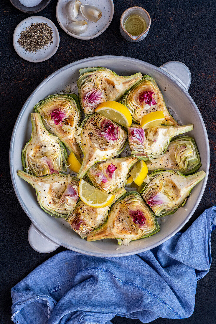 Quarters of artichokes and lemon slices in a round baking tin on a dark background