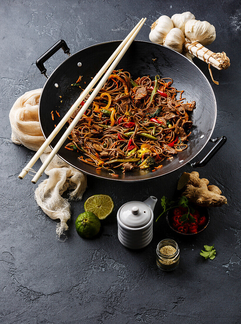 Asiatisches Fast Food Stir fry Nudeln Soba mit Rindfleisch und Gemüse in Wok-Pfanne auf dunklem Stein Hintergrund
