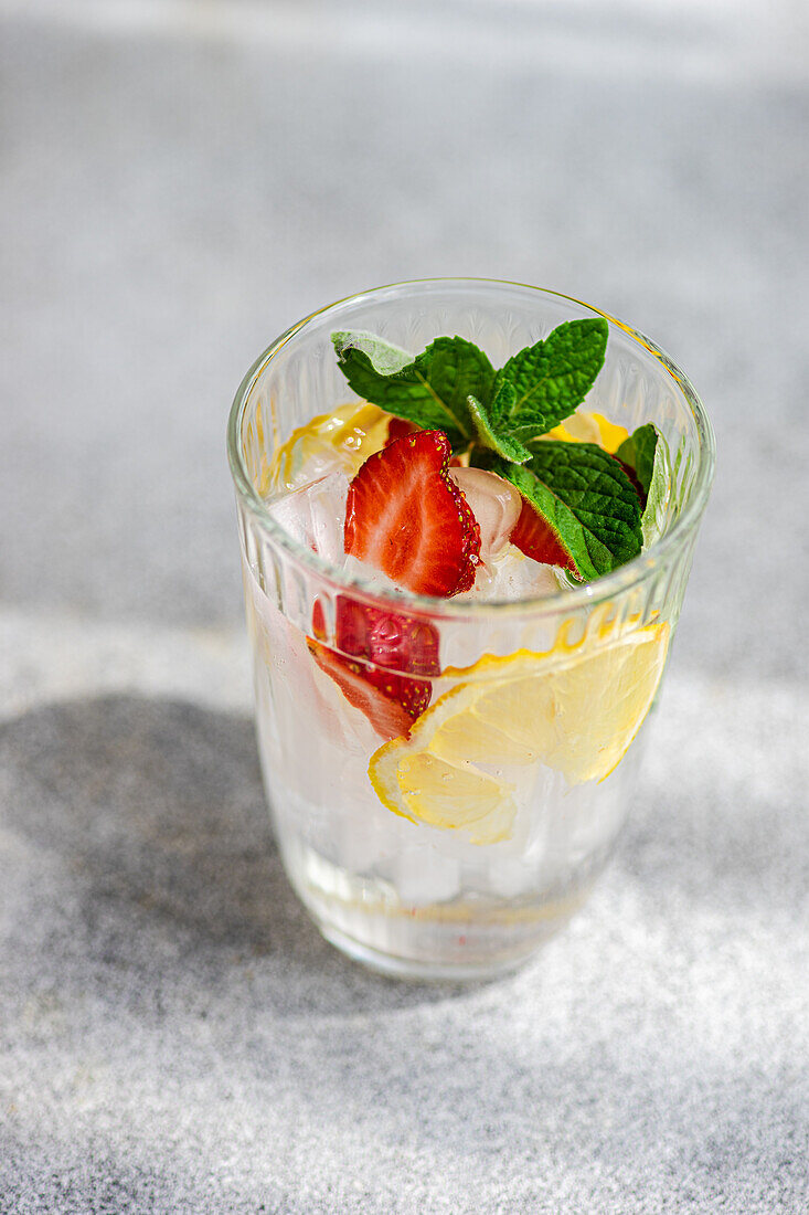 Summer cocktail glass with ice, mint, lemon and strawberry in the glass against blurred background in sunny day